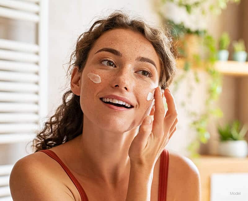 Young woman applying cream to her face